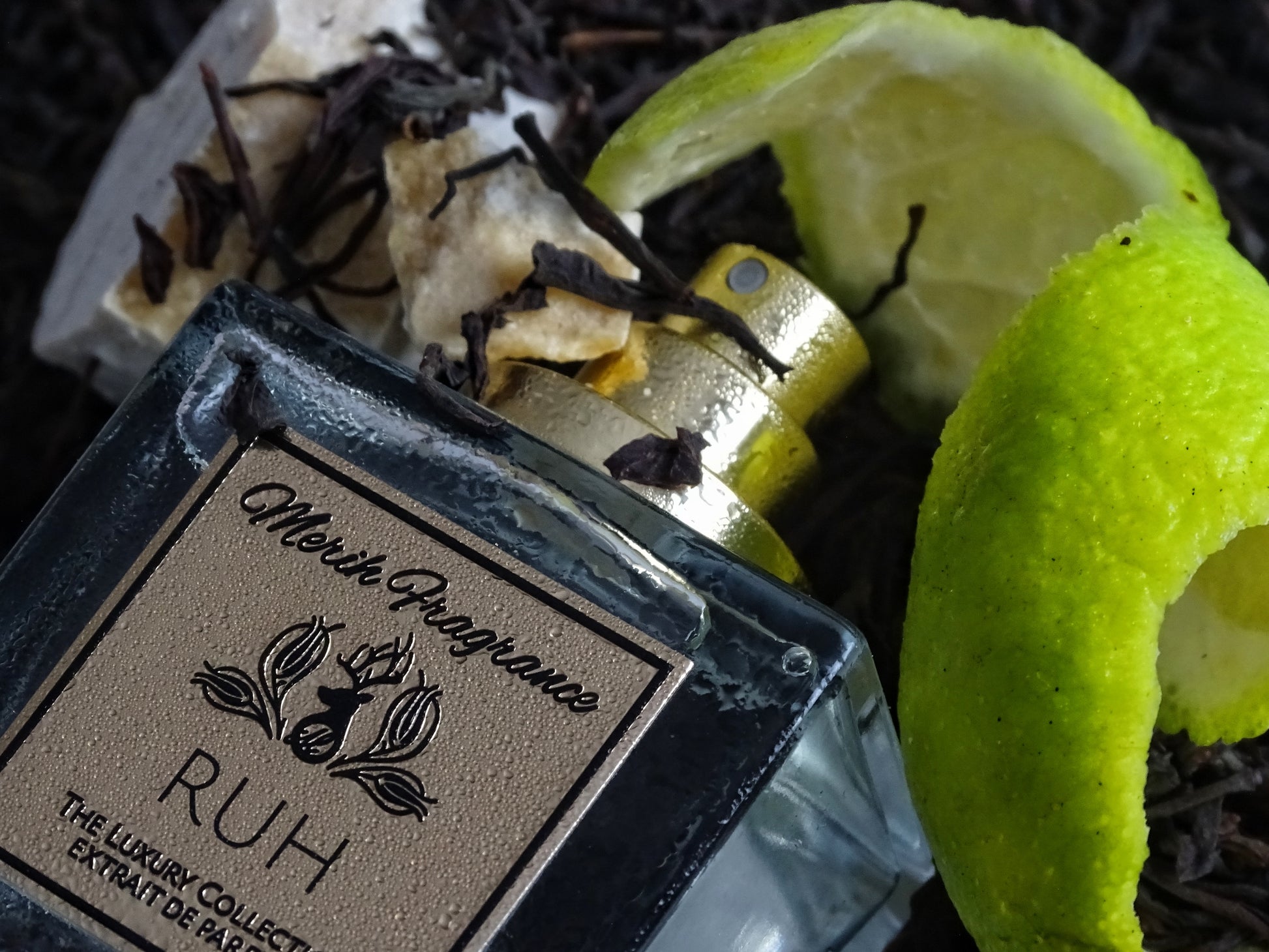 Merih Fragrance Ruh aus der Luxury Collection – Flakon ohne Kappe, mit sichtbarem Sprühkopf. Umgeben von weißem Moschus, schwarzem Tee und Bergamottenschalen. Fokus auf die geprägten Details des metallischen Labels. Das leicht angefeuchtete Glas unterstreicht den frischen Charakter des Dufts.